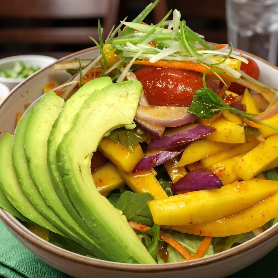 Close-up of a vibrant salad with sliced avocado, mango, red onion, cherry tomatoes, and green onions.
