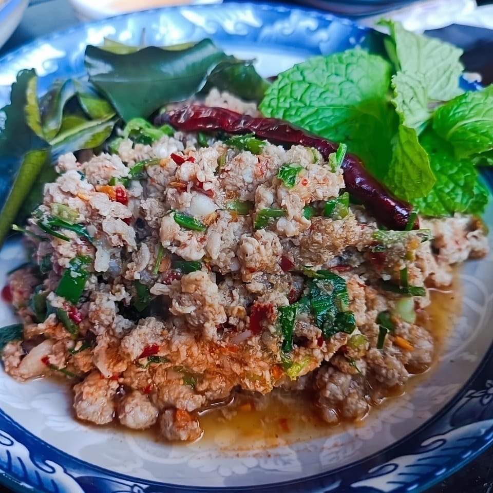 Spicy minced pork salad (Larb Moo) with herbs, dried chilies, and mint on a blue and white plate.