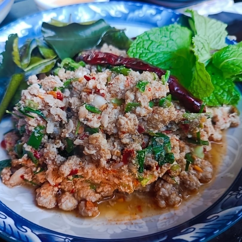 Spicy minced pork salad (Larb Moo) with herbs, dried chilies, and mint on a blue and white plate.