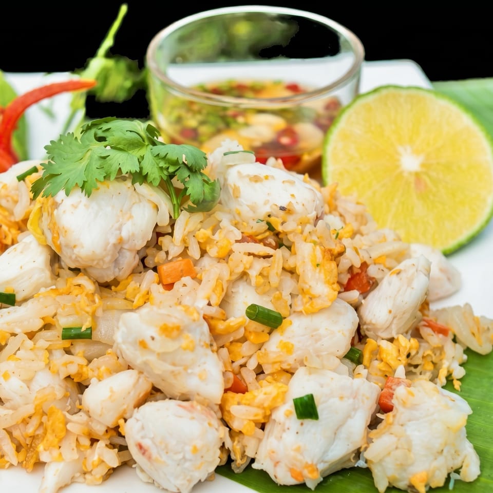 Crab fried rice with cilantro, lime, and chili sauce on a white plate.