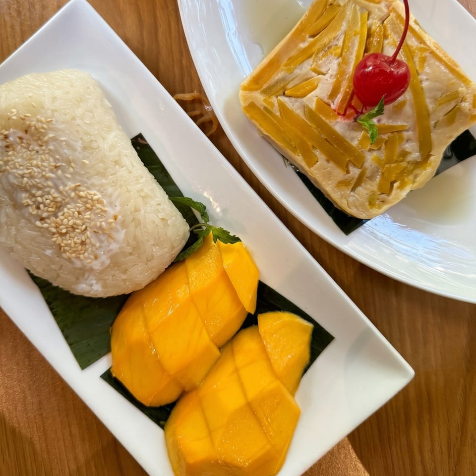 Mango sticky rice with sesame seeds and a pumpkin custard with a cherry on white plates.